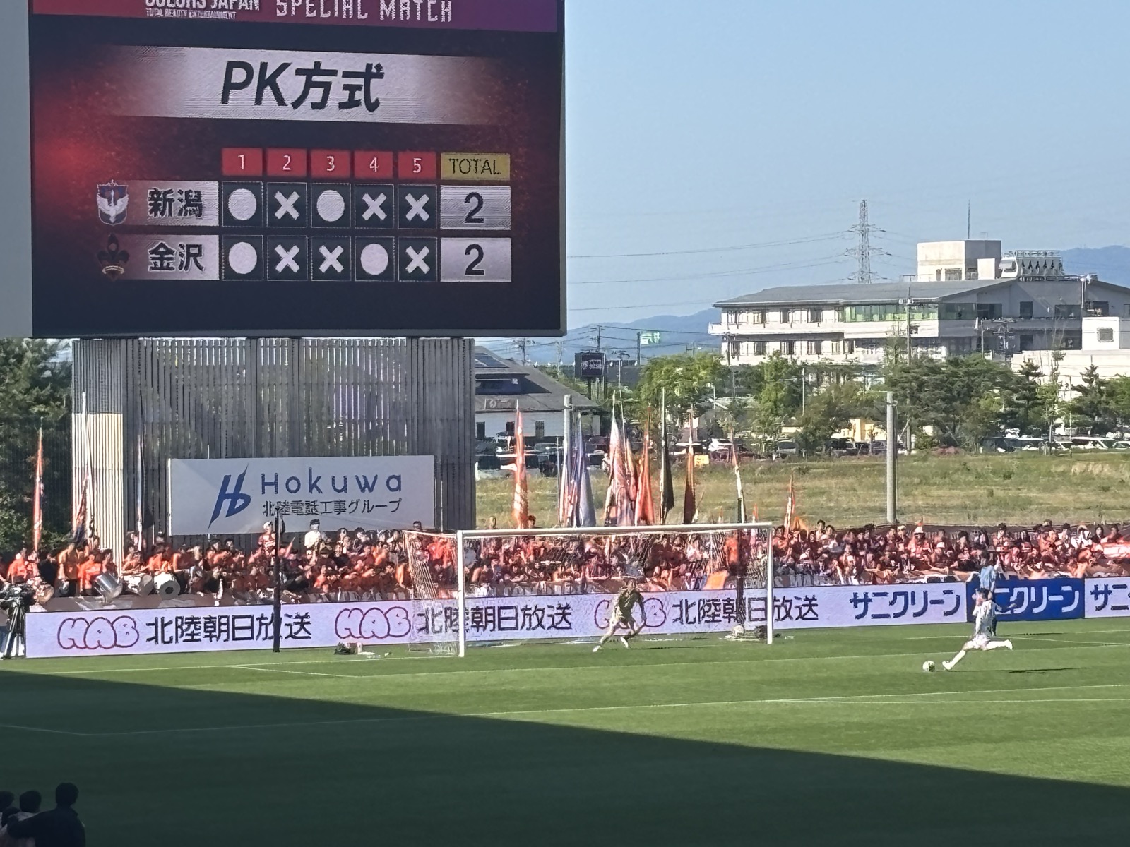 PK方式スコアボードと金沢ゴール前のPKキッカー(PK 2-2 同点)
