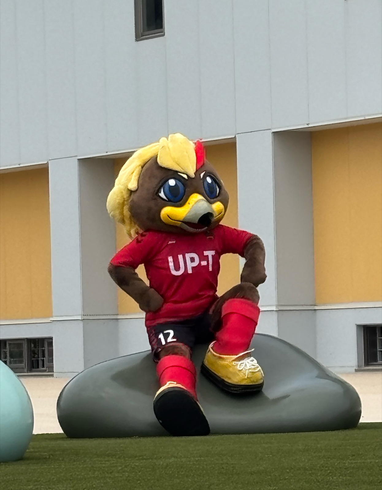 UP-Tユニフォーム姿のゲンゾーがスタジアム外で岩のオブジェに腰かけてポーズ