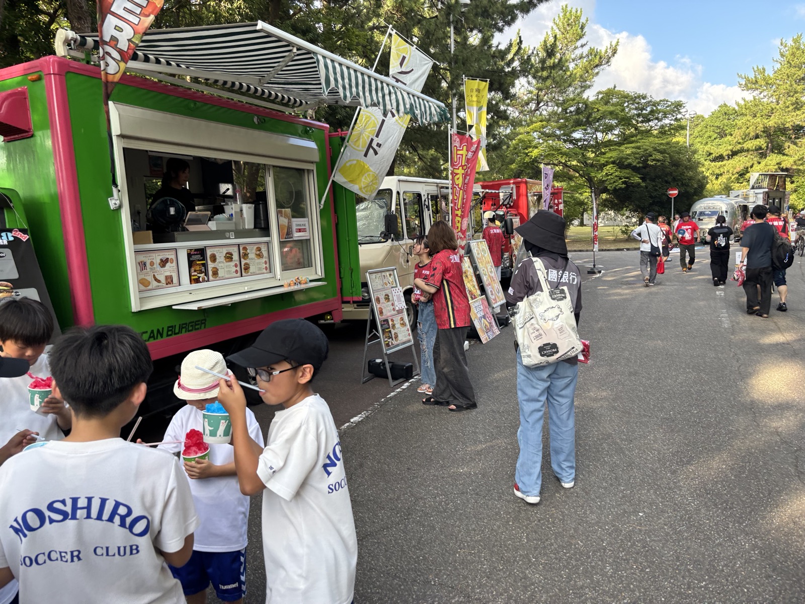 西部緑地公園陸上競技場前に並ぶキッチンカーと買い物をする親子連れ