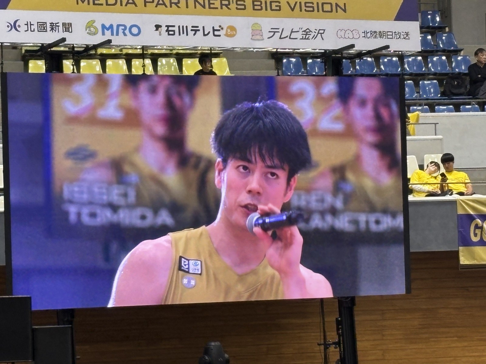 大型ビジョンに映ったマイクを持って話す富田一誠選手